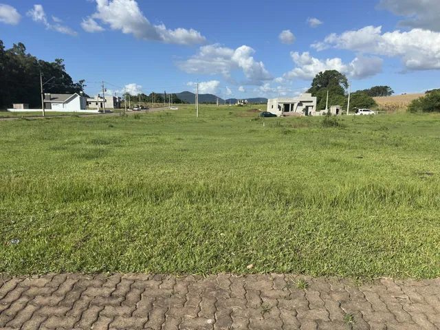 Vista externa de uma propriedade com campo gramado e construções ao fundo.
