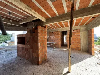 Vista interna de uma estrutura em construção com paredes de tijolo aparente e vigas de concreto.