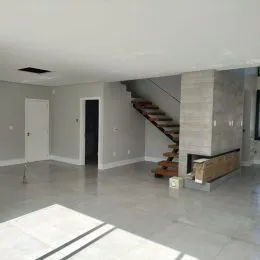 Vista interna de um ambiente com piso claro e escadaria visível.