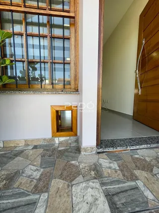 Vista interna de um corredor com piso de azulejo e moldura de janela de madeira.