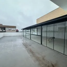 Vista de um espaço aberto com piso de concreto e grandes painéis de vidro.