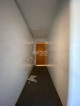 Hall de corredor interno com paredes brancas e porta de madeira.