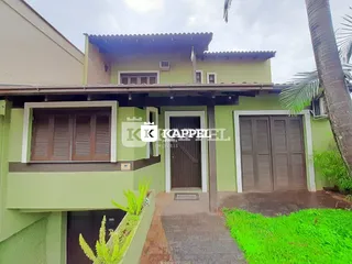Fachada externa de uma residência verde em Lajeado, Brasil, com detalhes em madeira e jardim na frente.