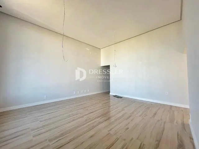 Vista interna de uma sala ampla com piso de madeira clara.