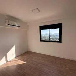 Ambiente interno com piso de madeira e janela mostrando uma vista externa.