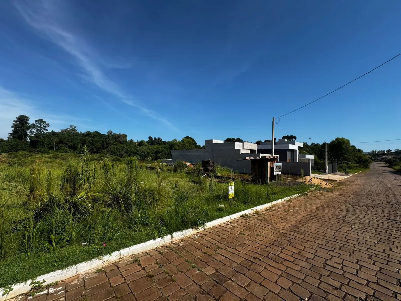 Vista da propriedade em Lajeado, Brasil, mostrando área de construção e vegetação ao lado de uma estrada.