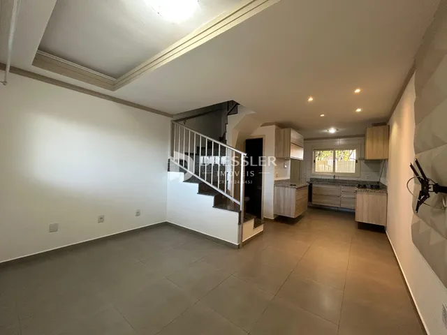 Ambiente interno de uma sala com acesso a uma cozinha e escadaria em uma residência.