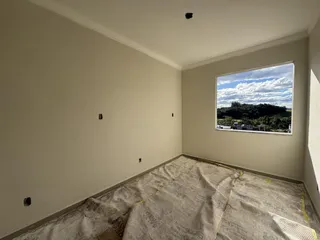 Vista interna de um cômodo com paredes claras e uma grande janela mostrando a paisagem externa.