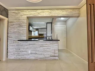 Interior de uma área comum com parede de pedra rústica e piso claro.