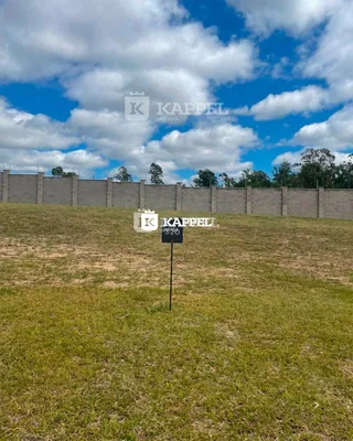 Vista externa de um campo gramado com cerca no fundo.