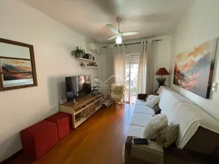 Sala de estar com piso de madeira, sofá branco e televisão.