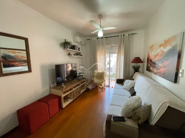 Sala de estar com piso de madeira, sofá branco e televisão.