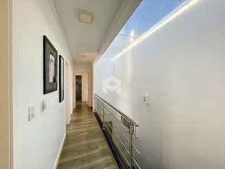 Foto do corredor interno de uma residência com piso de madeira e paredes brancas.