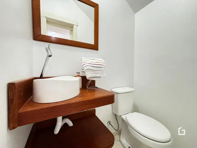 Foto de um banheiro com bancada de madeira e vaso sanitário branco.