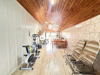 Uma sala longa com piso de madeira e uma área de jantar com cadeiras de vime.