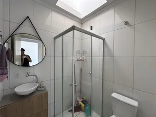 Banheiro com revestimento branco e box de vidro transparente.