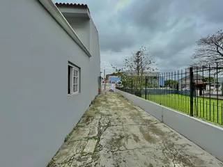 Vista lateral de uma propriedade com muro branco e quintal cercado.