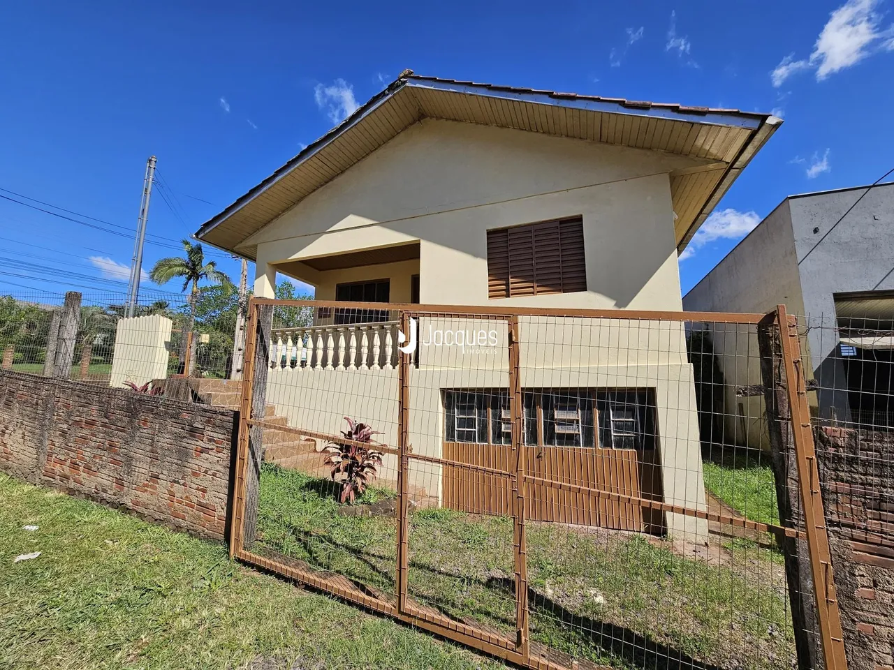 Fachada de uma casa em Lajeado, Brasil, com cerca de madeira e muro de tijolos.