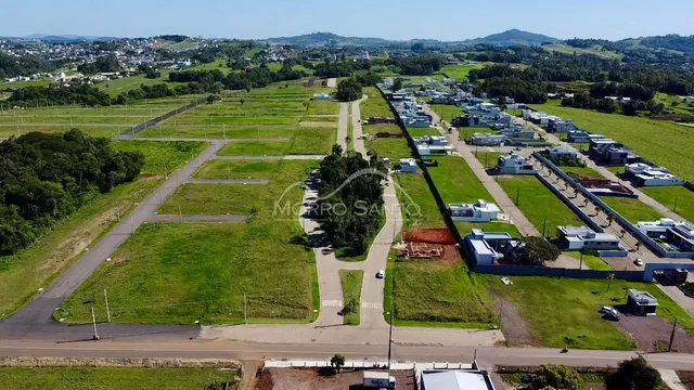 Vista aérea de um loteamento residencial com áreas verdes e casas no horizonte.