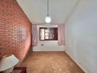Interior de um cômodo com parede de tijolos aparentes e piso cru.