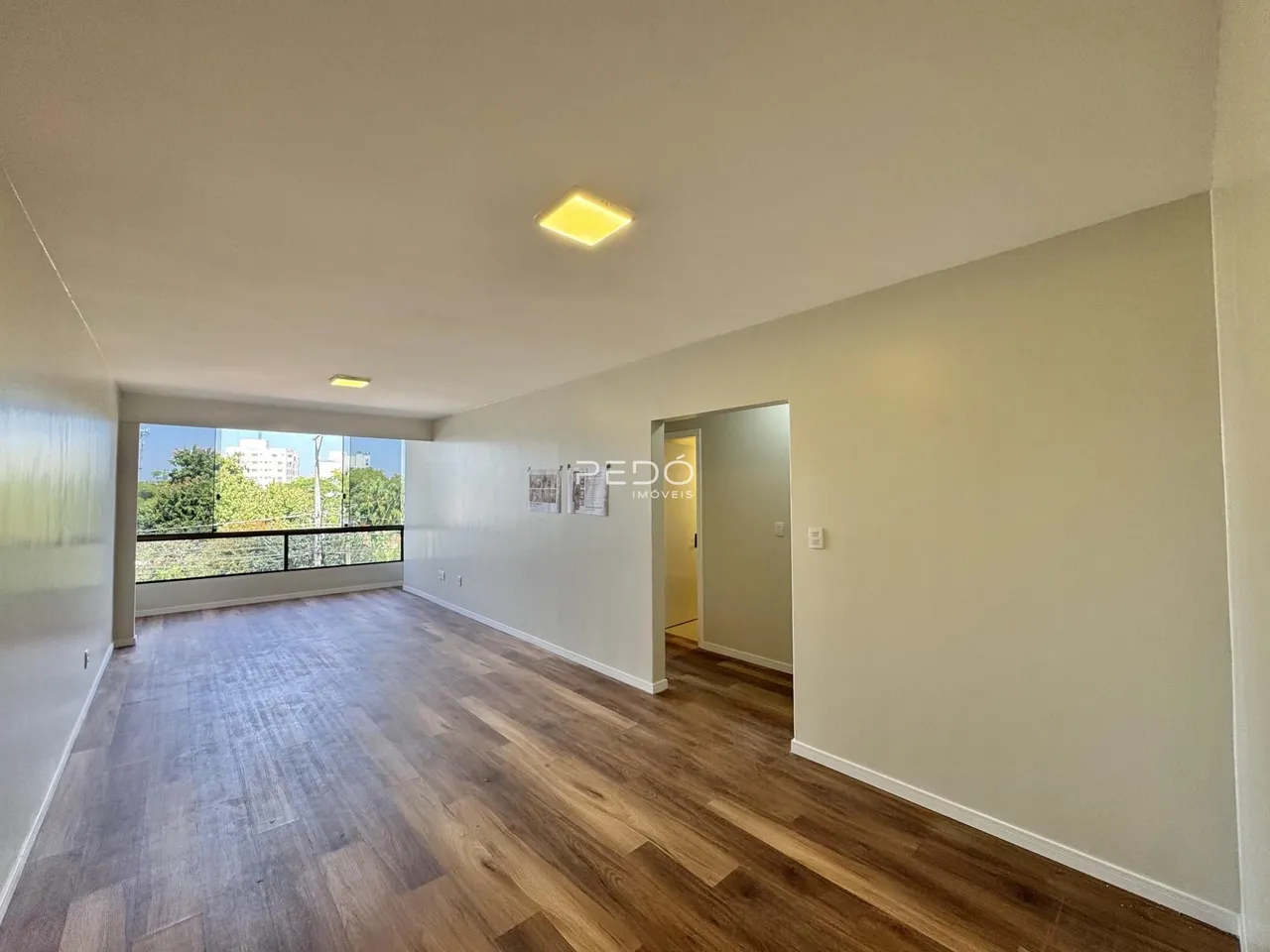 Sala de estar com piso de madeira clara e vista para o exterior.