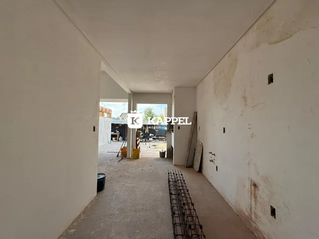 Hall de entrada com paredes brancas e piso de concreto em área de construção.