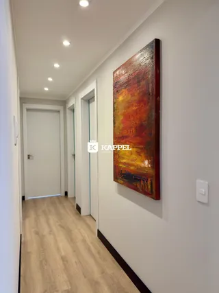 Um corredor interno com piso de madeira clara e uma pintura abstrata na parede.