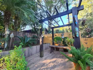 Vista externa de um jardim com deck de madeira e estrutura de pérgula.