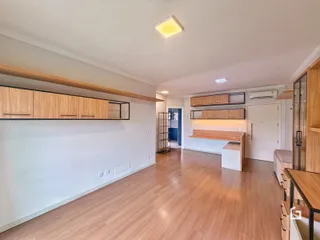 Ambiente interno de uma sala de estar com piso de madeira clara e armários em madeira.