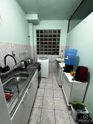 Uma foto interna mostra uma bancada de cozinha com pia e armários brancos.