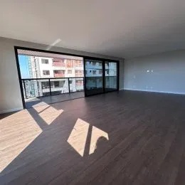 Sala de estar com piso de madeira escura e grandes janelas.