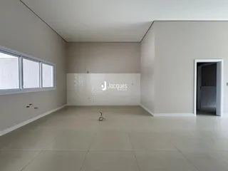 Ambiente interno de uma sala ampla com paredes brancas e piso claro.