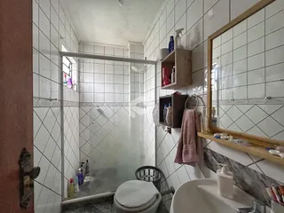 Banheiro com revestimento cerâmico e box de vidro.