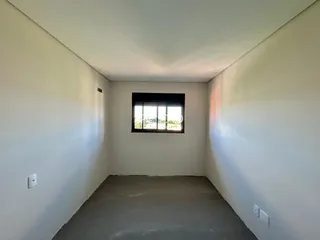 Vista interna de um cômodo vazio com paredes brancas e piso de concreto.