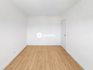 Uma sala ampla com piso de madeira clara e paredes brancas.