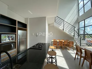 Interior de uma sala de estar e cozinha moderna com grandes janelas e escadaria.