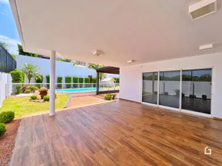 Vista de uma área externa coberta com piso de madeira que se abre para uma piscina e jardim.