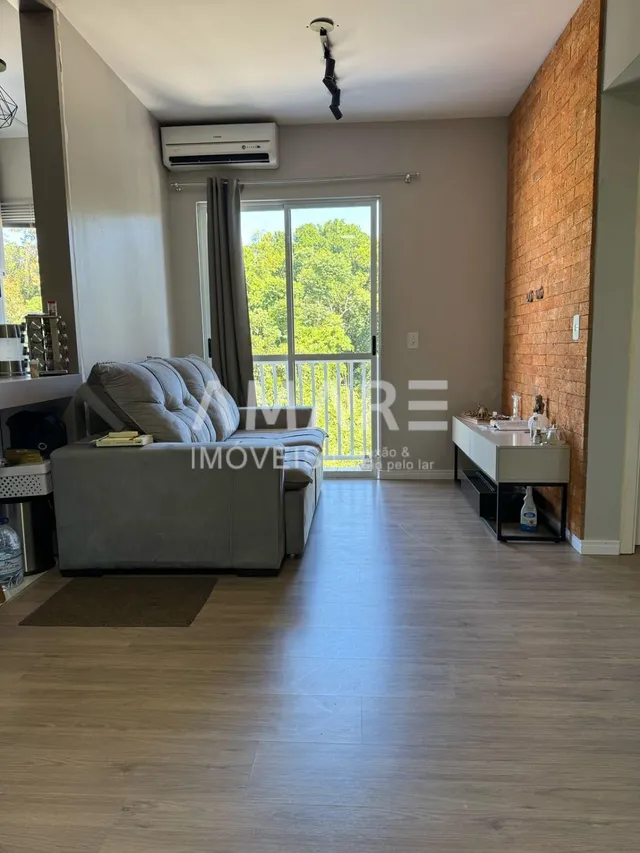 Sala de estar com sofá cinza e piso de madeira clara.