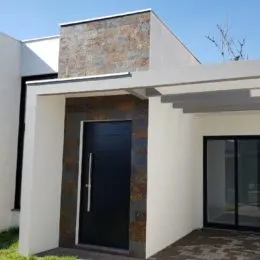 Fachada externa de uma residência moderna com revestimento de tijolo aparente e paredes brancas.
