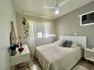 Quarto com cama de casal e janela com cortinas brancas.
