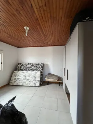 Quarto com cama e armário branco em ambiente com teto de madeira.