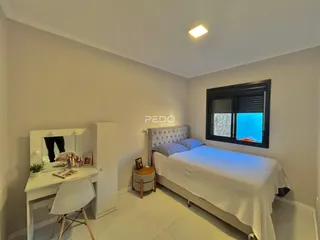 Quarto com cama e mesa de trabalho em ambiente claro.