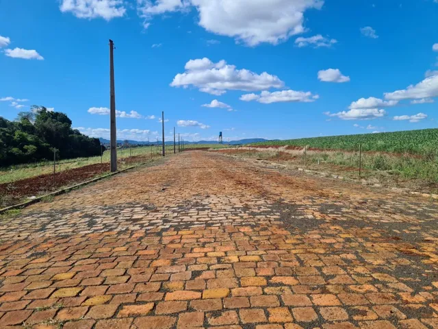 Vista de uma estrada de terra que se estende por um campo aberto sob um céu azul com nuvens.