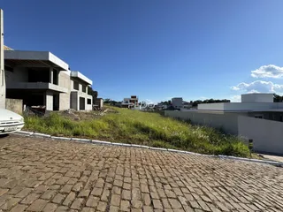 Vista externa de uma propriedade em construção com jardim e calçada de paralelepípedos.