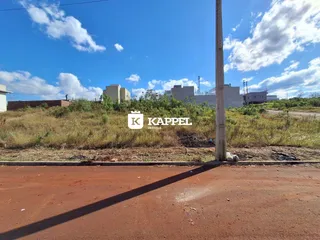 Vista externa de uma área com vegetação seca e construções ao fundo.