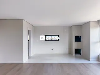Uma sala ampla e moderna com piso de madeira clara e televisão na parede.