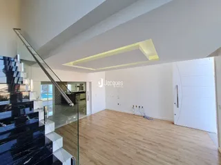 Interior de uma sala com piso de madeira e escadaria de vidro.