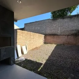 Vista externa de um pátio com piso de cascalho e parede de tijolos.