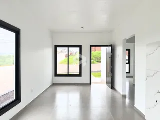 Interior de um espaço com paredes brancas e piso cinza claro, com grandes janelas voltadas para o exterior.