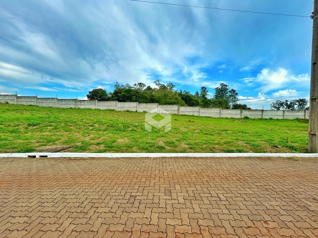 Vista externa de um terreno com cerca branca e vegetação verde.